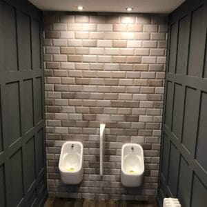 Various grey metro tile on a wall with two toilets in a restaurant bathroom