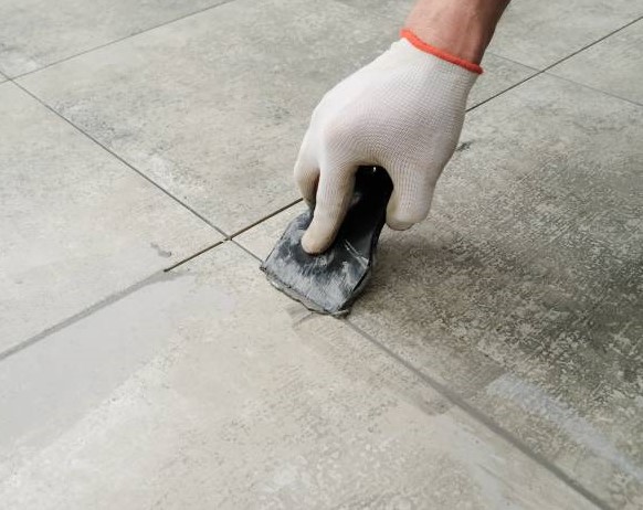 Grouting porcelain tiles. Tilers filling the space between tiles using a rubber trowel.