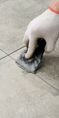 Grouting porcelain tiles. Tilers filling the space between tiles using a rubber trowel.